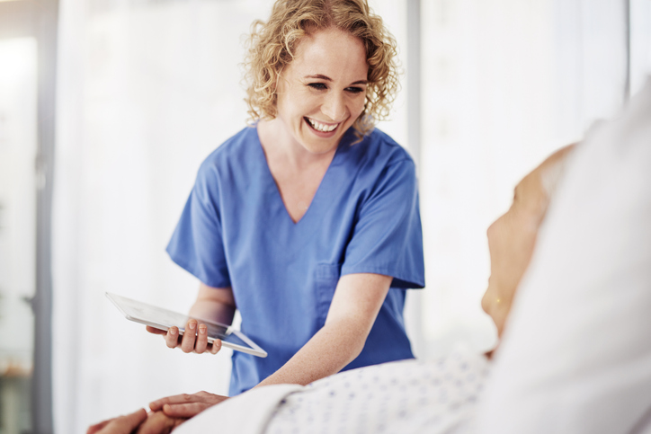 Smiling nurse holding tablet computer checks in on patient